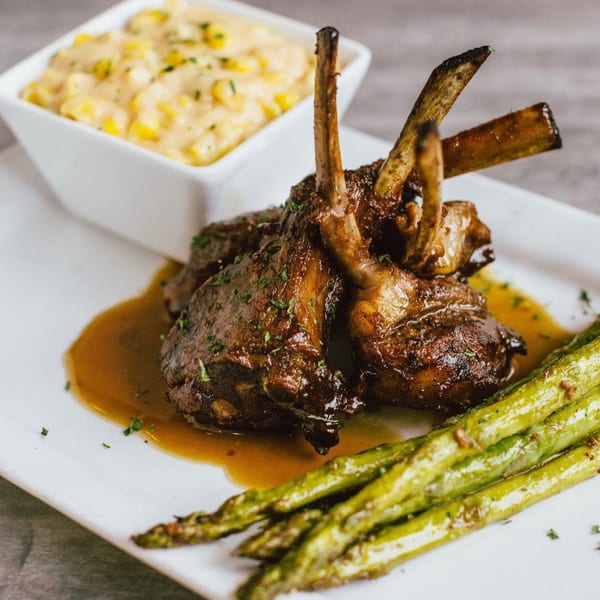 Soulé's lamb chops with gravy, asparagus, and a side of creamed corn on a white plate.