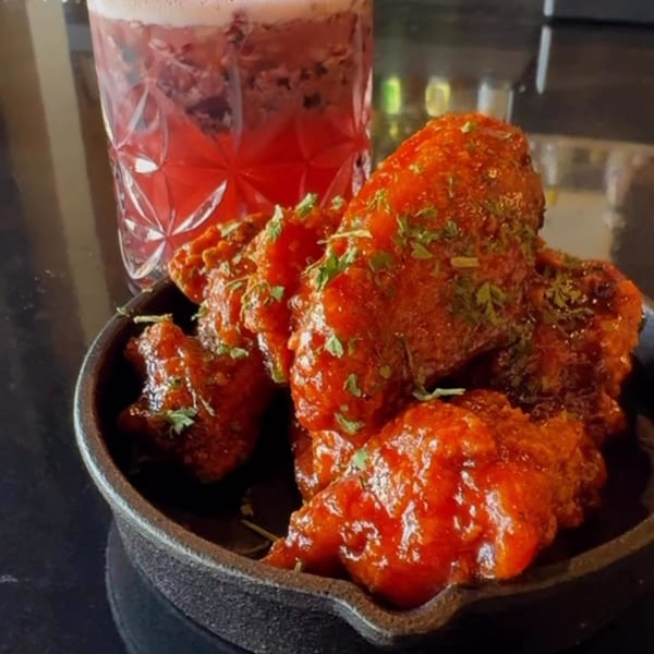 Soulé's red-sauced chicken wings in a cast iron dish, with a pink cocktail in the background.