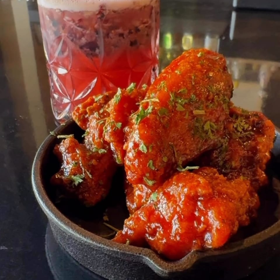 Soulé's red-sauced chicken wings in a cast iron dish, with a pink cocktail in the background.