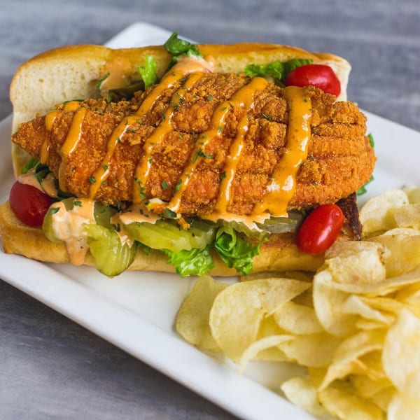 Soulé's fried chicken po'boy with sauce, lettuce, pickles, tomatoes, and a side of chips.