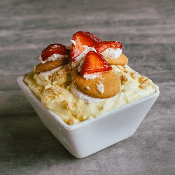 Soulé's banana pudding dessert with vanilla wafers, whipped cream, and fresh strawberries in a white bowl.