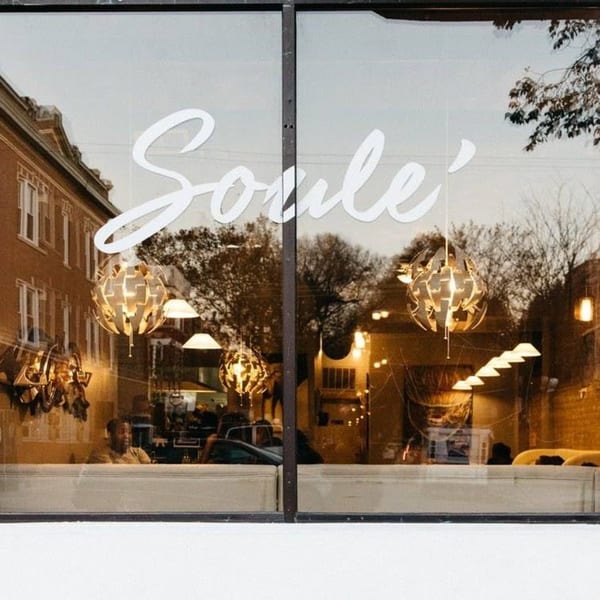The Soulé restaurant storefront at dusk, with its name on the window and warm interior lighting visible.