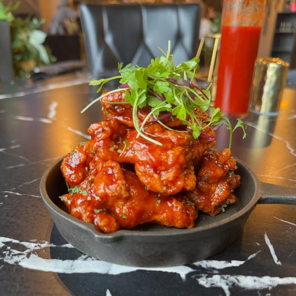 Soulé's spicy glazed chicken wings, garnished with fresh herbs, served in a cast iron skillet.