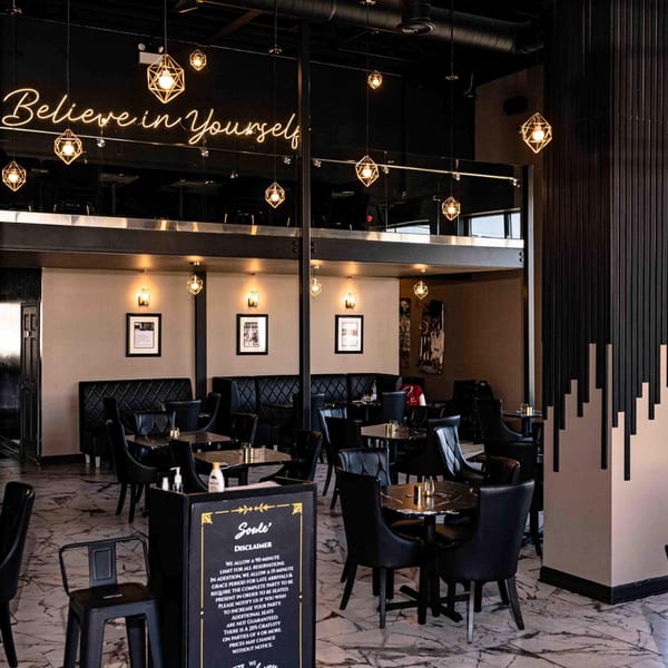 Soulé restaurant interior with black tables, chairs, booths, and a neon "Believe in Yourself" sign.