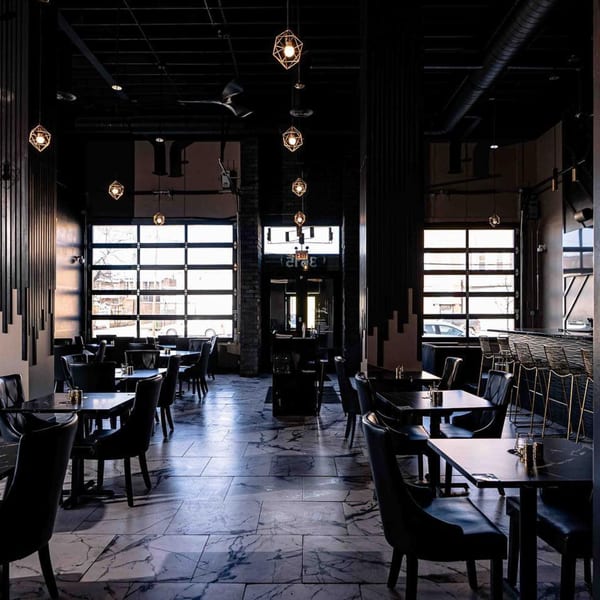 Soulé restaurant interior with dark tables, chairs, geometric pendant lights, and large windows.