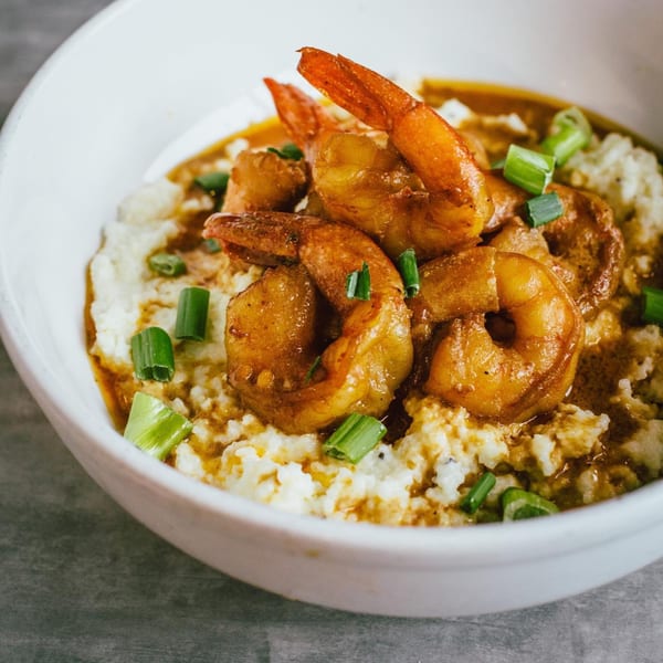 Soulé's shrimp and grits, topped with green onions, served in a white bowl.